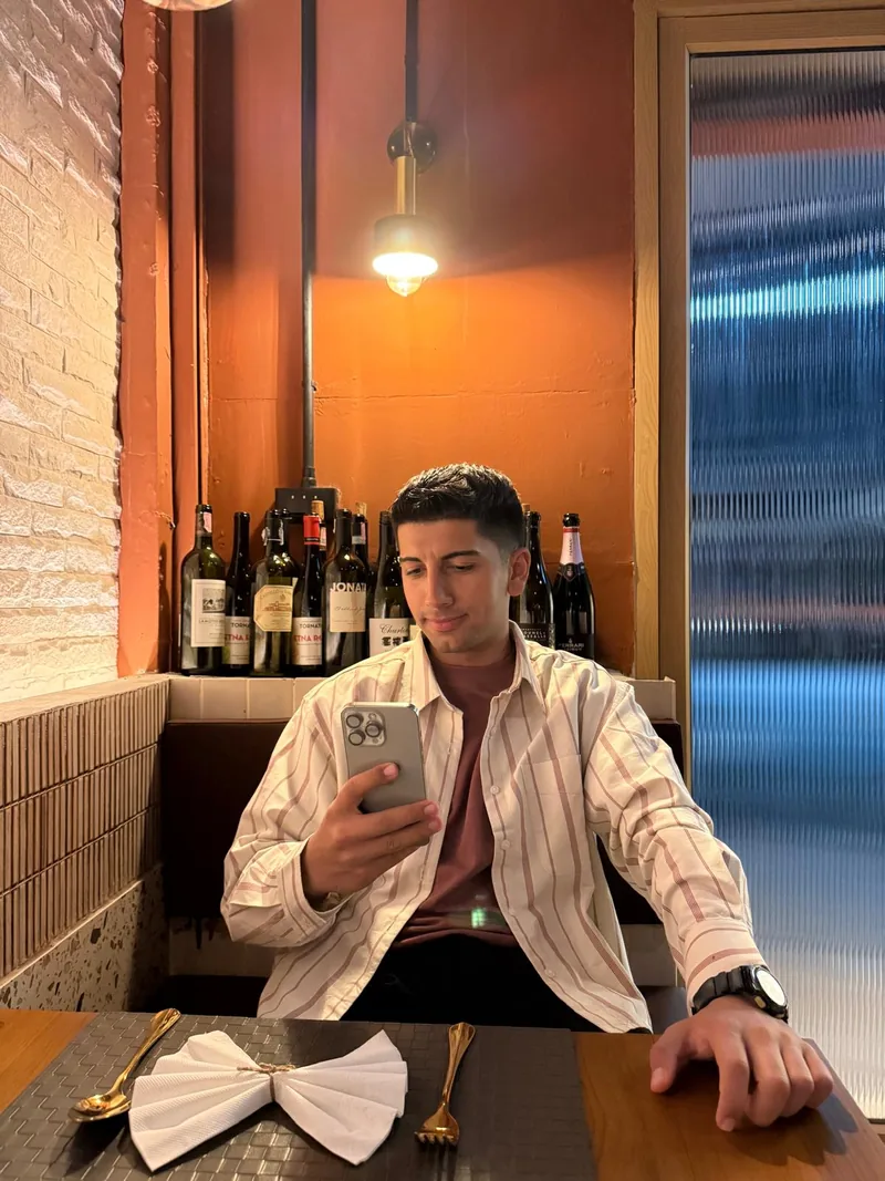ยีกิตผมสั้นสีเข้มนั่งอยู่ในร้านอาหารแสงไฟอบอุ่นและกำลังดูโทรศัพท์
