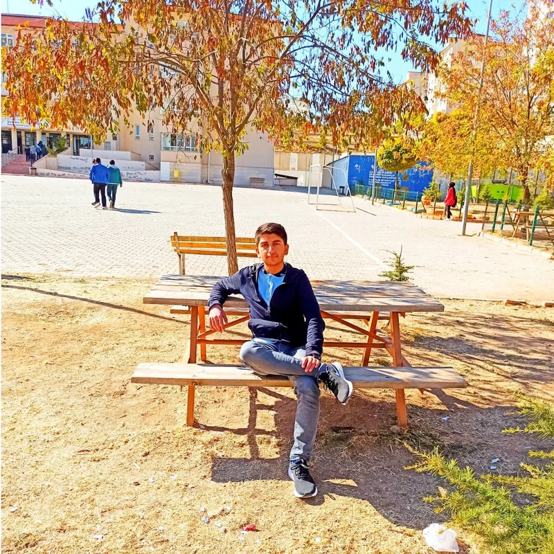 Yiğit นั่งอยู่บนม้านั่งปิกนิกในลานฤดูใบไม้ร่วง