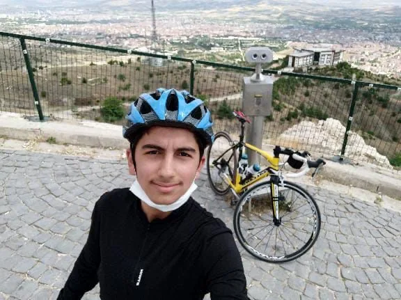 Yiğit in a bike helmet at a hillside overlook, a road bike behind him