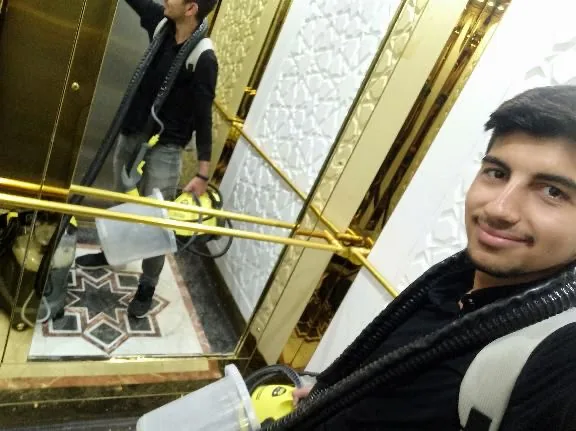 Yiğit carrying a yellow cleaning machine in a gold-trimmed elevator