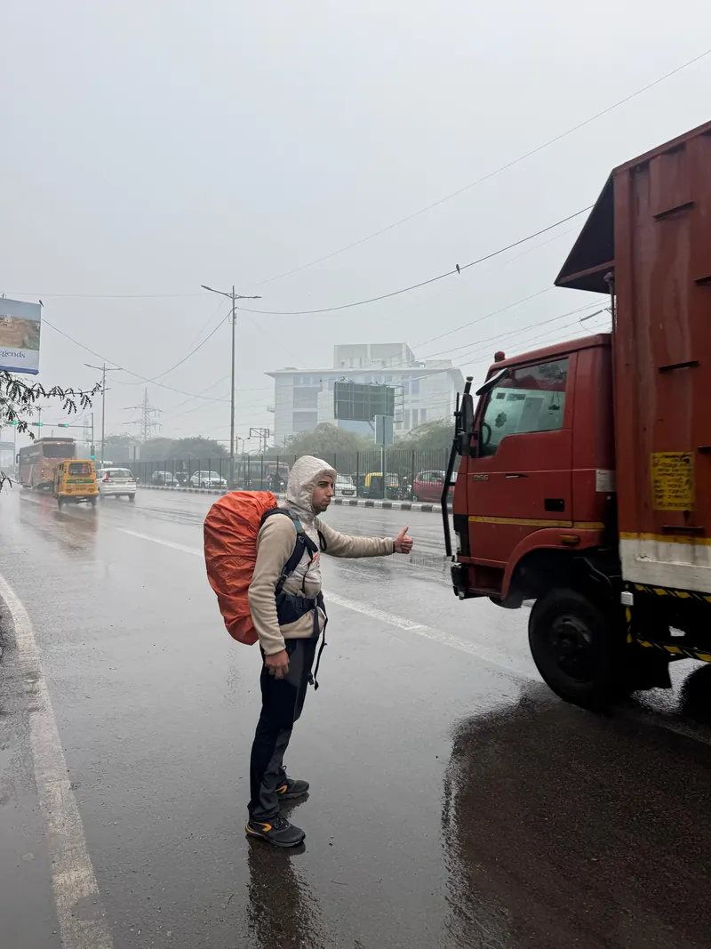 Yiğit hitchhiking in the rain with an orange pack